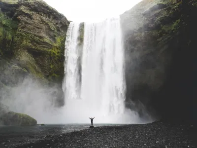 A huge waterfall in the background and a small figure standing at the bottom, raising their arms.